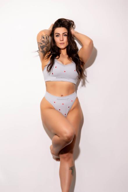 Jesse Rae from Babestation stand against a white wall wearing two piece grey underwear