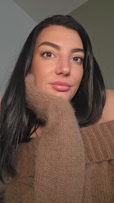 Mia Rosea rest her chin on her hand in a selfie while wearing a brown jumper