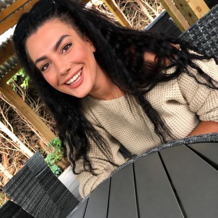 Mia Rosea sits smiling at an outdoor table wearing a jumper
