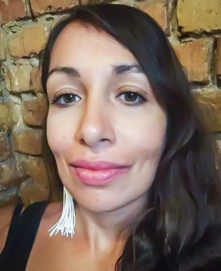 Rosa Freya takes a headshot selfie wearing dangly ear rings on a brick wall background