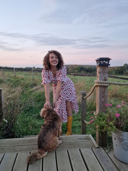 Sasha Fire from Babestation outdoors in a field wearing polka dot summer dress and yellow wellies petting a dog