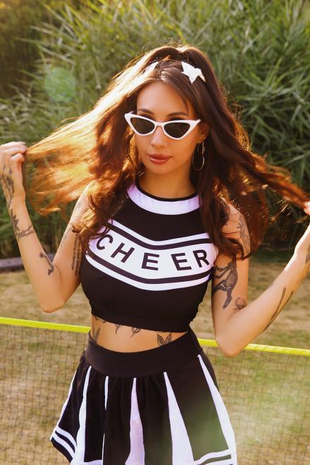 Live cam model Zeena Valvona throws her hair to both sides wearing a black and white cheerleader outfit and point white sunglasses