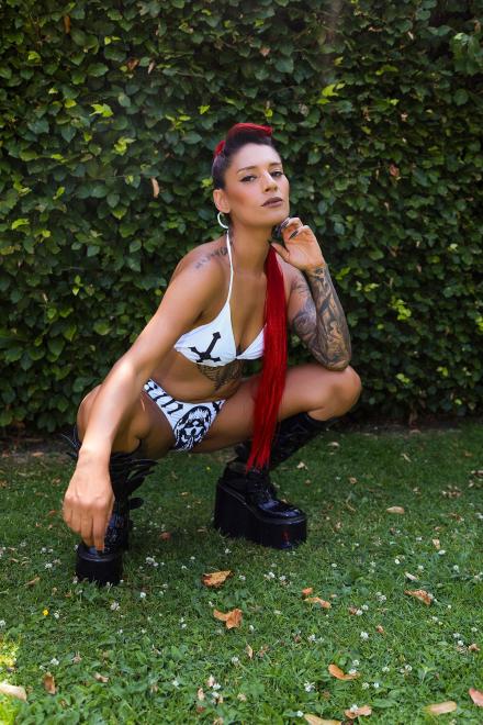 Live cam girl Valkyrie Awakens squats on the grass by a tall busy wearing white bikini with antichrist pattern and knee high black boots Live cam girl Valkyrie Awakens squats on the grass by a tall busy wearing white bikini with antichrist pattern and knee high black boots