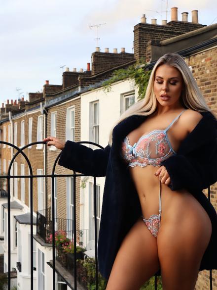 Live cams model Macy Kate stands by a railing on a London rooftop with terrace housing in the background